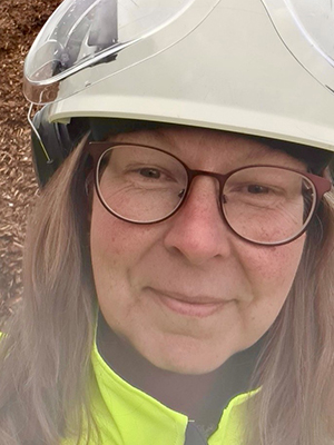 En kvinna med skyddshjälm ser in i kameran, hon ser glad ut